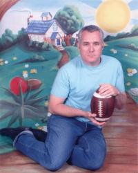 R.M. Vaughan seated on floor against colourful backdrop, holding football